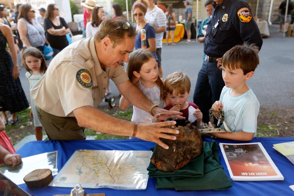 California State Parks interpretive specialist Dave Duplantier shows children a stump from Sugarloaf Ridge State Park that was hollowed out by flames during the Nuns Fire but appears intact on the outside, at the Sonoma Plaza Farmers Market in Santa Rosa, California, on Tuesday, July 24, 2018. (Alvin Jornada / The Press Democrat)