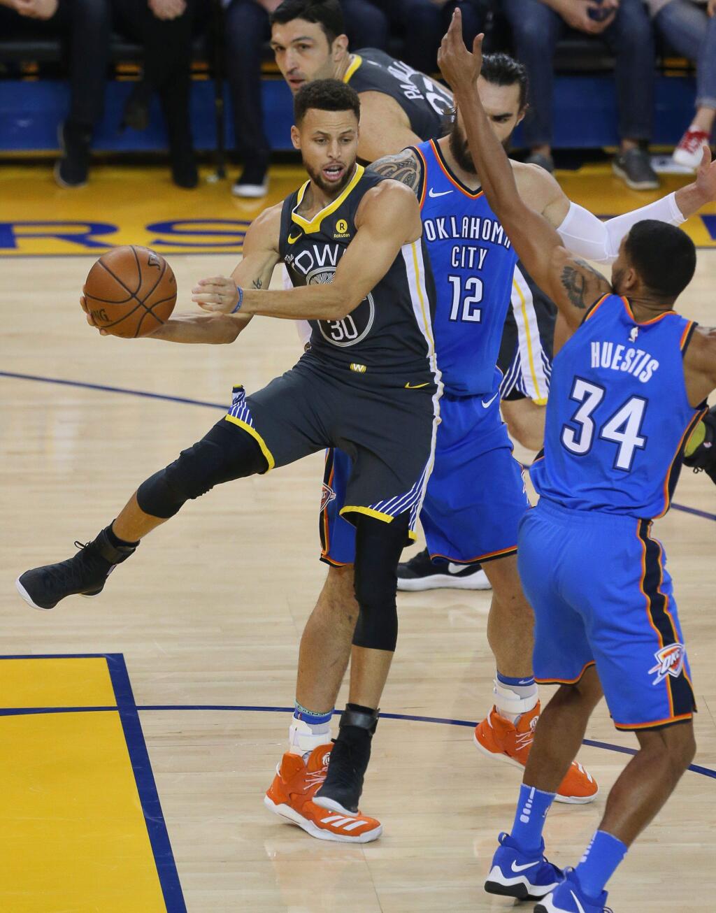 Golden State Warriors guard Stephen Curry dishes off a pass around Oklahoma City Thunder forward Josh Huestis during their game in Oakland on Tuesday, February 6, 2018. (Christopher Chung/ The Press Democrat)