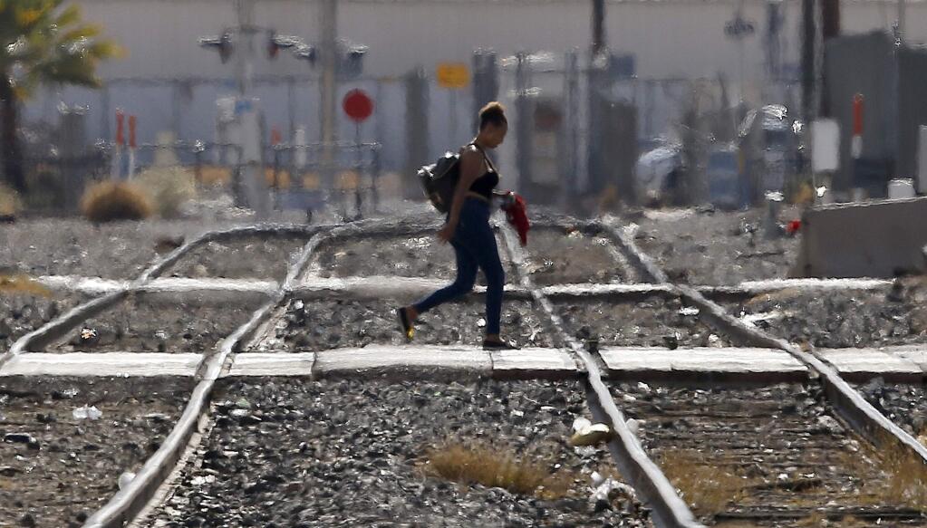 While the heat waves rise up from the ground, a woman crosses the railroad tracks as temperatures climb past 112-degrees Thursday, July 5, 2018, in Phoenix. (AP Photo/Ross D. Franklin)