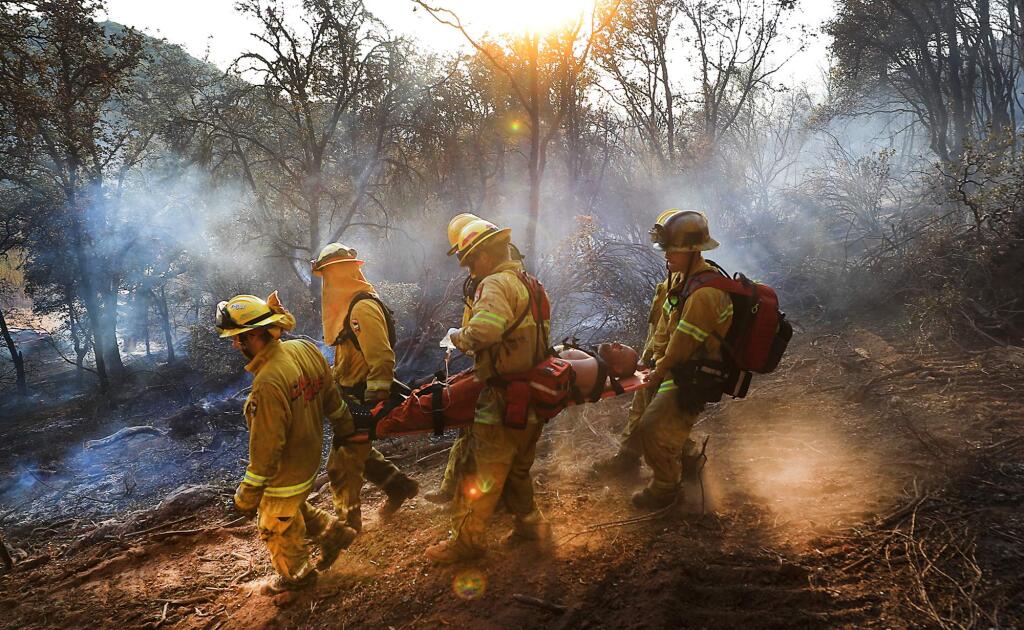Cal Fire and Lakeport firefighters carry an injured inmate firefighter along the fire line at the Bottle fire in Kelseyville on Aug. 8, 2017. (KENT PORTER / The Press Democrat) 2017