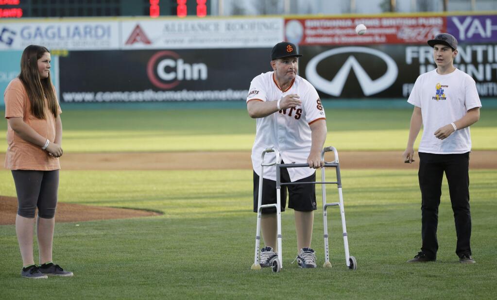 Bryan Stow, center, throws out the ceremonial first pitch as his children Tabitha, left, and Tyler watch during the San Jose Giants' minor league baseball home opener Thursday, April 16, 2015, in San Jose, Calif. Stow was left brain damaged after an attack outside Dodger Stadium in Los Angeles in 2011. (AP Photo/Marcio Jose Sanchez)