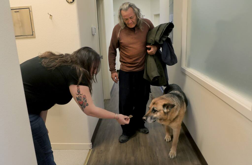 Russian River Health Center medical assistant Vanessa Woodbyrne offers up a treat to Moxie after handler Jesse Hagan, a Sycamore Court resident, flooded from his trailer and later a friends apartment, had a check-up at the recently reopened flood damaged clinic in Guerneville, Friday, March 15, 2019. (Kent Porter / The Press Democrat) 2019