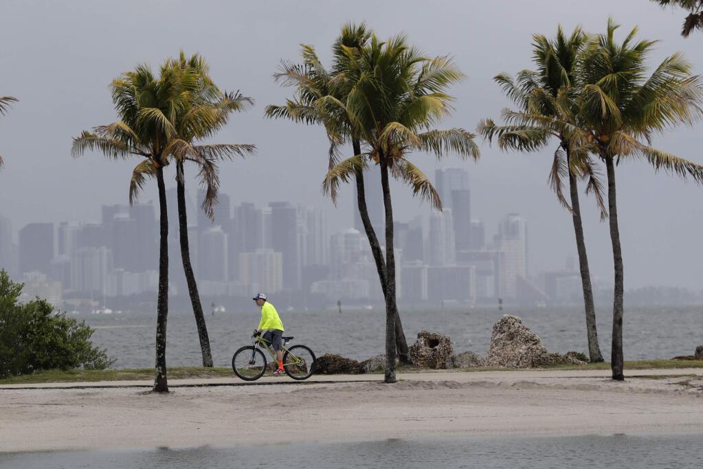 FILE - In this May 15, 2020, photo, the Miami skyline is shrouded in clouds as a cyclist rides along Biscayne Bay at Matheson Hammock Park, in Miami. National Oceanic and Atmospheric Administration's Climate Prediction Center, said Thursday, May 21, 2020, that six to 10 of the storms could develop into hurricanes, with winds of at least 74 mph. They're also predicting that three to six of those could develop into major hurricanes. (AP Photo/Lynne Sladky, File)