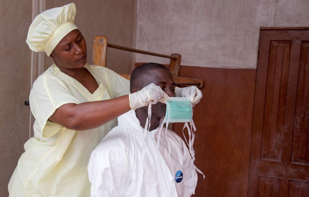 In this photo taken on Tuesday, Aug. 12, 2014, a healthcare worker, left, helps a colleague as she prepares his Ebola personal protective equipment before entering the Ebola isolation ward at Kenema Government Hospital. (AP Photo/ Michael Duff)