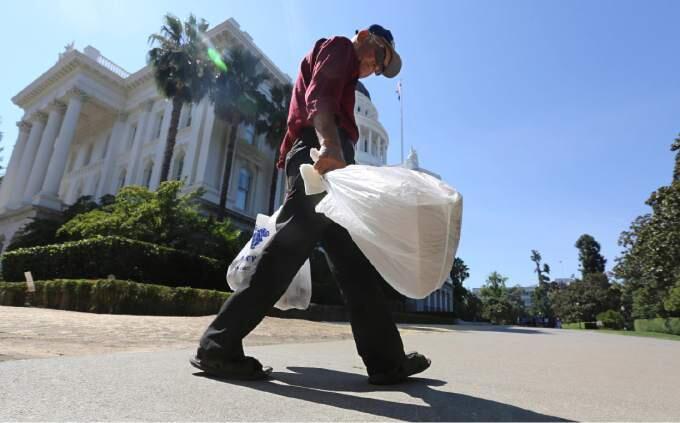 FILE - In this Aug. 12, 2014 file photo, a man carries plastic single-use bags past the State Capitol in Sacramento, Calif. Election officials said Monday, Feb. 23, 201 that a trade group had turned in enough signatures to qualify a referendum on California?s plastic bag ban law, suspending implementation of the nation?s first statewide ban until voters weigh in on the November 2016 ballot. (AP Photo/Rich Pedroncelli, File)