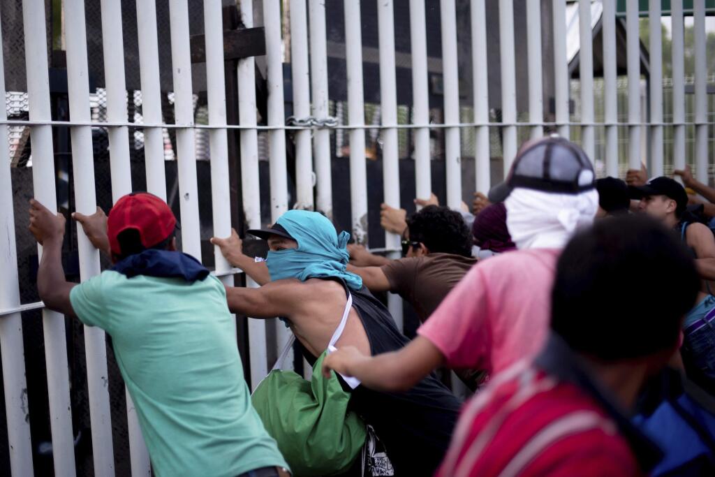 Central American migrants try to force their way through a customs gate at the border bridge connecting Guatemala and Mexico, in Tecun Uman, Sunday, Oct. 28, 2018. A new group of migrants, who called themselves a second caravan, gathered on a bridge after forcing their way through a gate at the Guatemalan end and clash with Mexican authorities. (AP Photo/Santiago Billy)