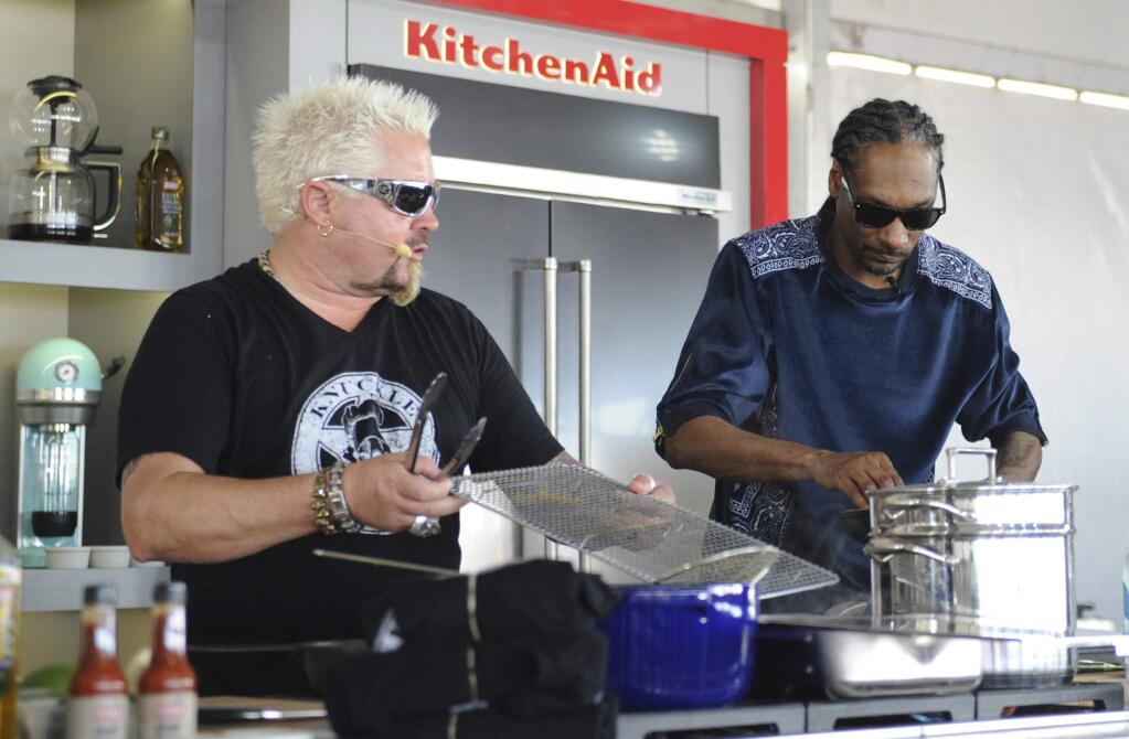 This Feb. 26, 2017 photo made available by WorldRedEye.com, shows rapper Snoop Dog, right, and Chef Guy Fieri, cooking together during a demonstration at the South Beach Wine & Food Festival in Miami Beach, Fla. Rappers Snoop, Action Bronson and Rev Run are ushering the culinary world into an era where shows like ““Martha and Snoop's Potluck Dinner Party” are a hit and rappers like 2 Chainz drop cookbooks along with their albums. (Ryan Troy/WorldRedEye.com via AP)