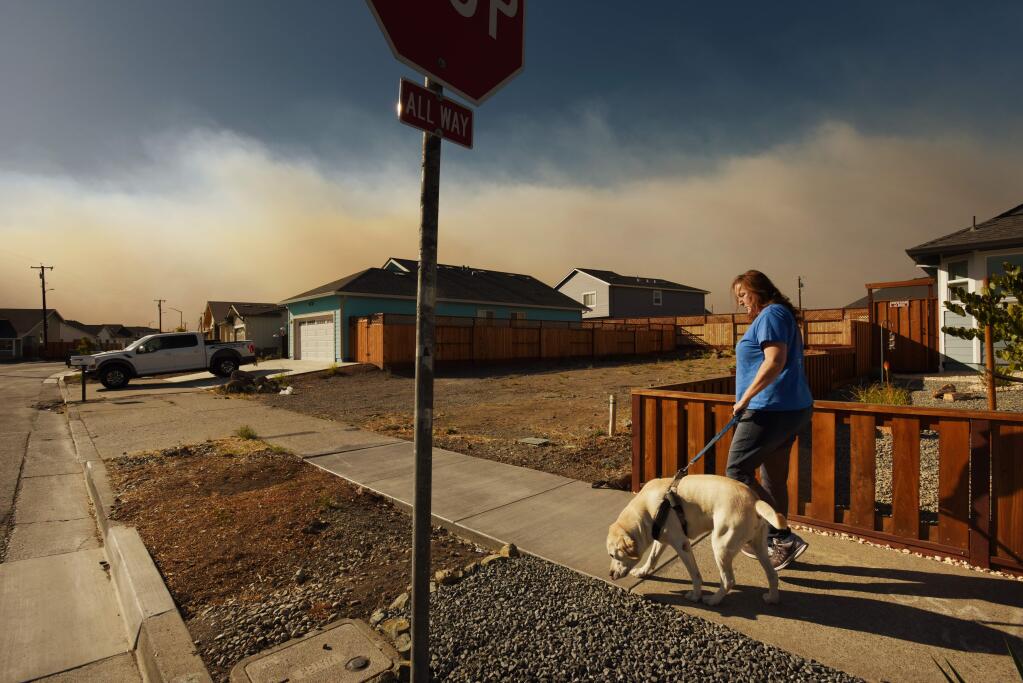 Tricia Woods walking her dog Jack towards her home on Hopper Avenue while a stream of thick smoke from the Kincade Fire flows just north of her Coffey Park neighborhood in Santa Rosa, California. Woods admits to sleeping poorly since the start of the Kincade Fire and of also having deep empathy for those currently losing their homes to the blaze. October 27, 2019.(Photo: Erik Castro/for The Press Democrat)