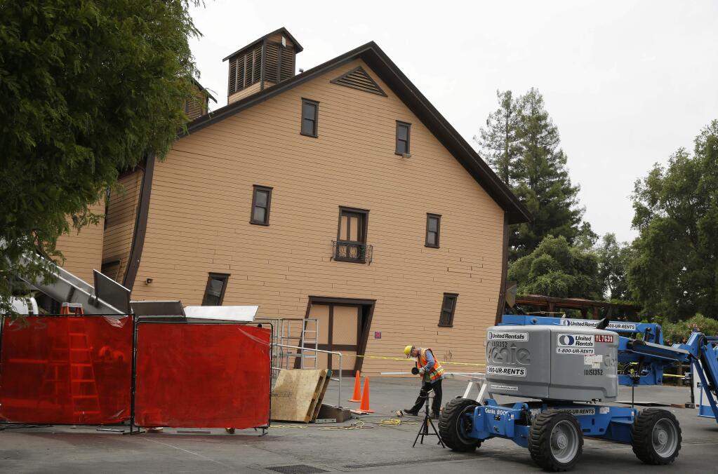 In this photo taken Friday, Aug. 29, 2014, a worker in hard hat and vest is shown with the leaning earthquake damaged historic winery building in the background dating from 1886 at Trefethen Family Vineyards in Napa, Calif. The first grapes of the season came in the winery as they always do, tumbling out of the big bins in a shower of glistening purple rain. But there was something a little bit different. This harvest, workers are wearing bright orange safety vests and yellow hard hats, safety measures made necessary by the fact that the wineryís historic building which once stood proudly above the grape-crushing operations now sags at the knees like a fighter whoís taken one punch too many, legacy of the Aug. 24 major earthquake. (AP Photo/Eric Risberg)