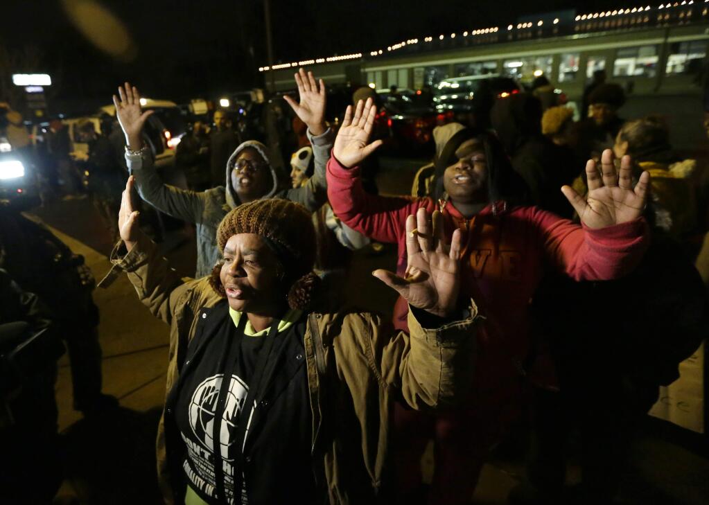 Barbara Jones, joined by other protesters, raises her hands, Monday, Nov. 24, 2014, in Ferguson, Mo., more than three months after an unarmed black 18-year-old man was shot and killed there by a white policeman. Ferguson and the St. Louis region are on edge in anticipation of the announcement by a grand jury whether to criminally charge Officer Darren Wilson in the killing of Michael Brown. (AP Photo/Charlie Riedel)