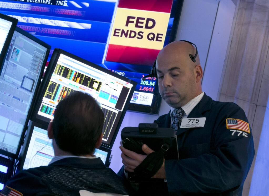 Trader Fred DeMarco, right, works on the floor of the New York Stock Exchange, as a television screen shows the decision of the Federal Reserve, Wednesday, Oct. 29, 2014. The Fed plans to keep a key interest rate at a record low to support a U.S. job market that's improving but still isn't fully healthy and help lift inflation from unusually low levels. As expected, it's also ending a bond purchase program that was intended to keep long-term rates low. (AP Photo/Richard Drew)