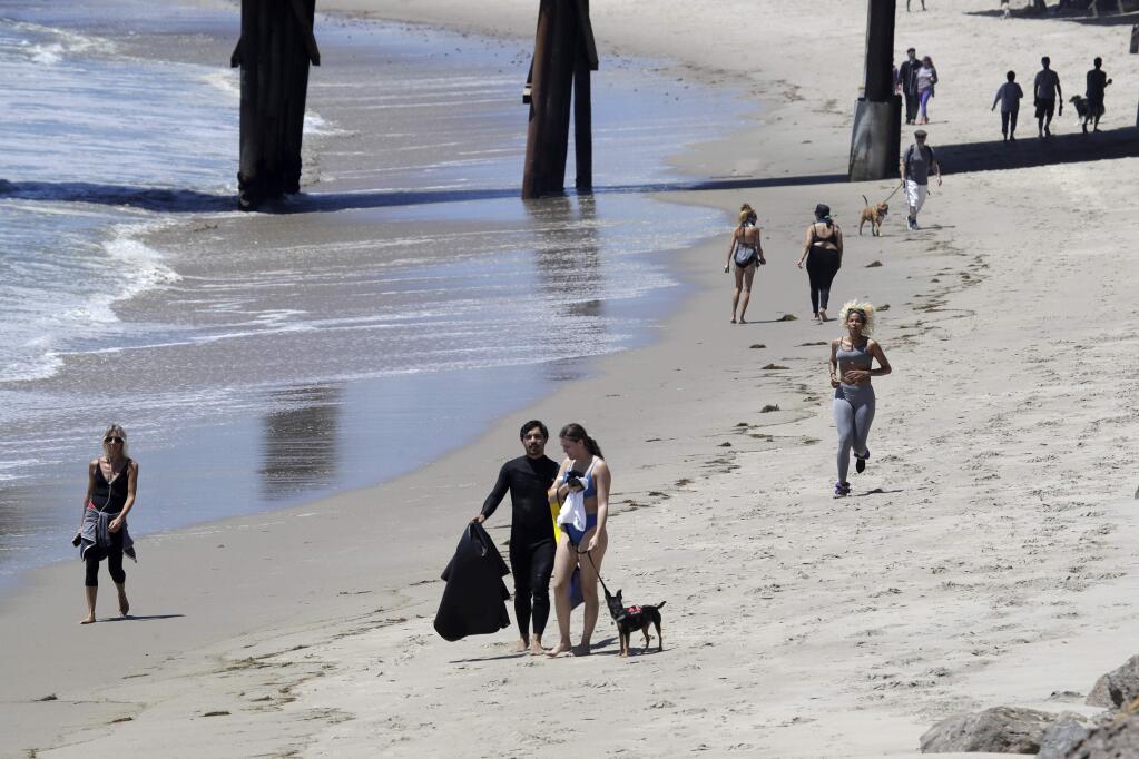 FILE - In this Wednesday, May 13, 2020, file, photo beachgoers walk and exercise on the beach in Malibu, Calif. Masks are required at Los Angeles County beaches, which reopened Wednesday to join counterparts in other states that have allowed a somewhat limited return to famed stretches of sand. (AP Photo/Marcio Jose Sanchez, File)