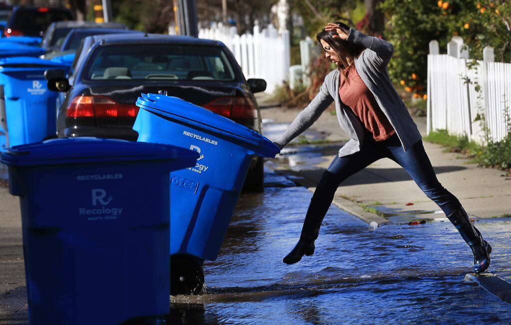 Channah Zeldin moves her recycling bin before it floats away as water from a sheared fire hydrant cascades down the street, Monday, Jan. 21, 2019 at the corner of West Eighth and Prince Streets in Santa Rosa. (Kent Porter / Press Democrat) 2019