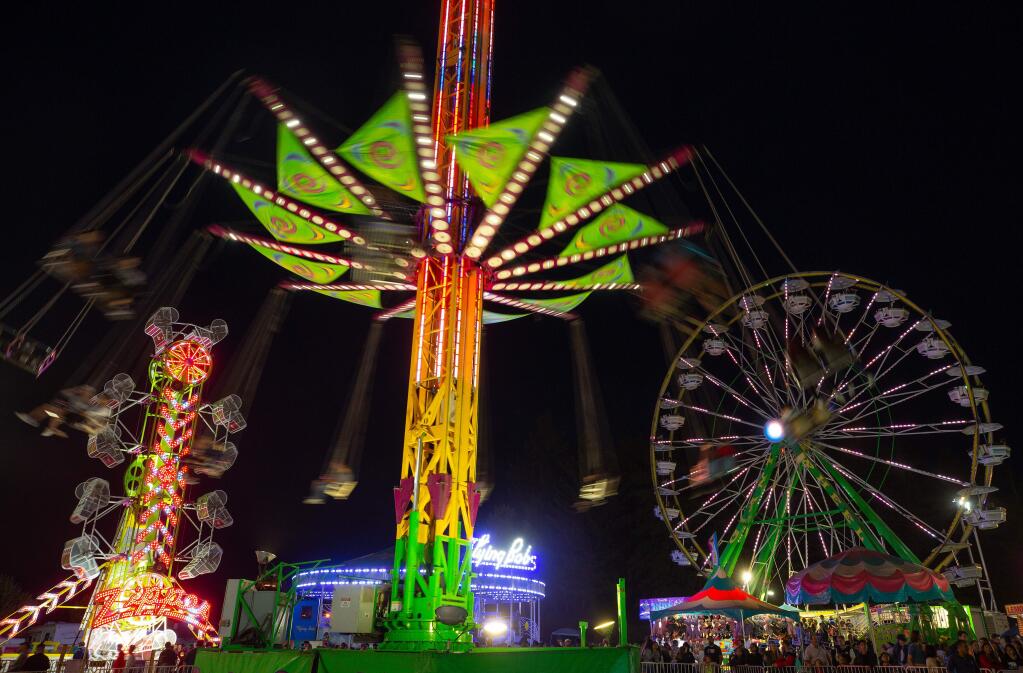 The swings of the Vertigo, center, slowly spin downward with the Zipper and Giant Wheel towering over the Midway crowds during the last weekend of the Sonoma County Fair, in Santa Rosa, California, on Friday, August 9, 2019. (Alvin Jornada / The Press Democrat)