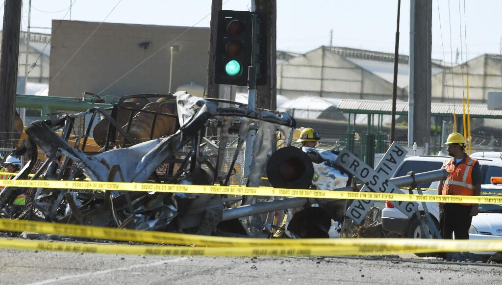 A worker stands next to a railroad crossing sign and the wreckage of a truck that was struck by a Metrolink passenger train that then derailed Tuesday, Feb. 24, 2015, in Oxnard, Calif. Three cars of the Metrolink train tumbled onto their sides, injuring dozens of people in the town 65 miles northwest of Los Angeles. (AP Photo/Mark J. Terrill)