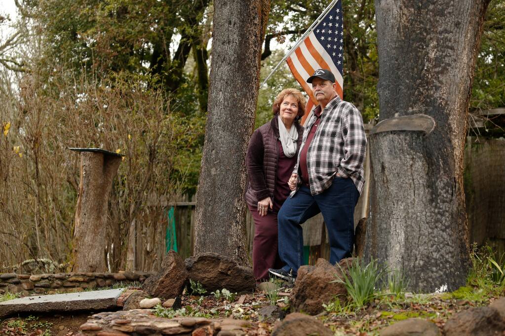 Sandi and Dave Cavanaugh stand for a portrait between two trees on their property that still bear burn marks from the Tubbs fire which destroyed their home of 26 years, off Mark West Springs Road, in Santa Rosa, California. Photographed on Friday, Jan. 11, 2019. (ALVIN JORNADA/ PD)