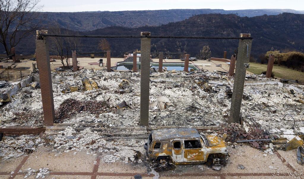 FILE - In this Dec. 3, 2018 file photo, a vehicle rests in front of a home leveled by the Camp Fire in Paradise, Calif. Authorities estimate it will cost at least $3 billion to clear debris of 19,000 homes destroyed by California wildfires last month. State and federal disaster relief officials said Tuesday, Dec. 11, 2018, that private contractors will most likely begin removing debris in January from Butte, Ventura and Los Angeles counties and costs are likely to surpass initial estimates. (AP Photo/Noah Berger, File)
