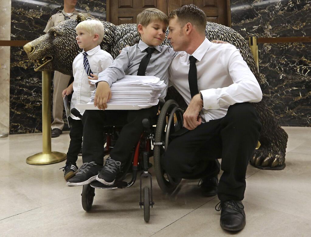 Otto Coleman, 6, waits outside the Governors office with his brother Fenton, 4, left, and father Joshua, to deliver a stack of petitions with thousands of signatures calling on California Gov. Jerry Brown to veto a measure requiring nearly all California school children to be vaccinated Monday, June 29, 2015, in Sacramento, Calif. (AP Photo/Rich Pedroncelli)