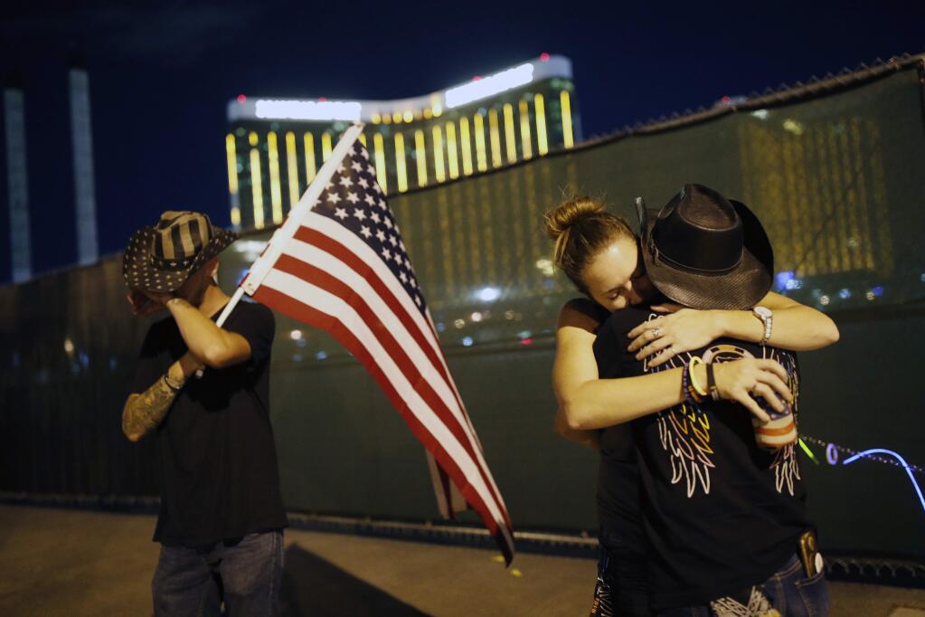 FILE - In this Oct. 1, 2018, file photo, Megan Murphy, right in hat, embraces Cara Knoedler as Kenneth Wright wipes his eyes on the first anniversary of the mass shooting in Las Vegas. In the two years since the deadliest mass shooting in modern U.S. history, the federal government and states have taken some action to tighten gun regulations. But advocates say they're frustrated more hasn't been done since the attack in Las Vegas killed 58 people on Oct. 1, 2017, and that mass shootings keep happening across the country. (AP Photo/John Locher, File)