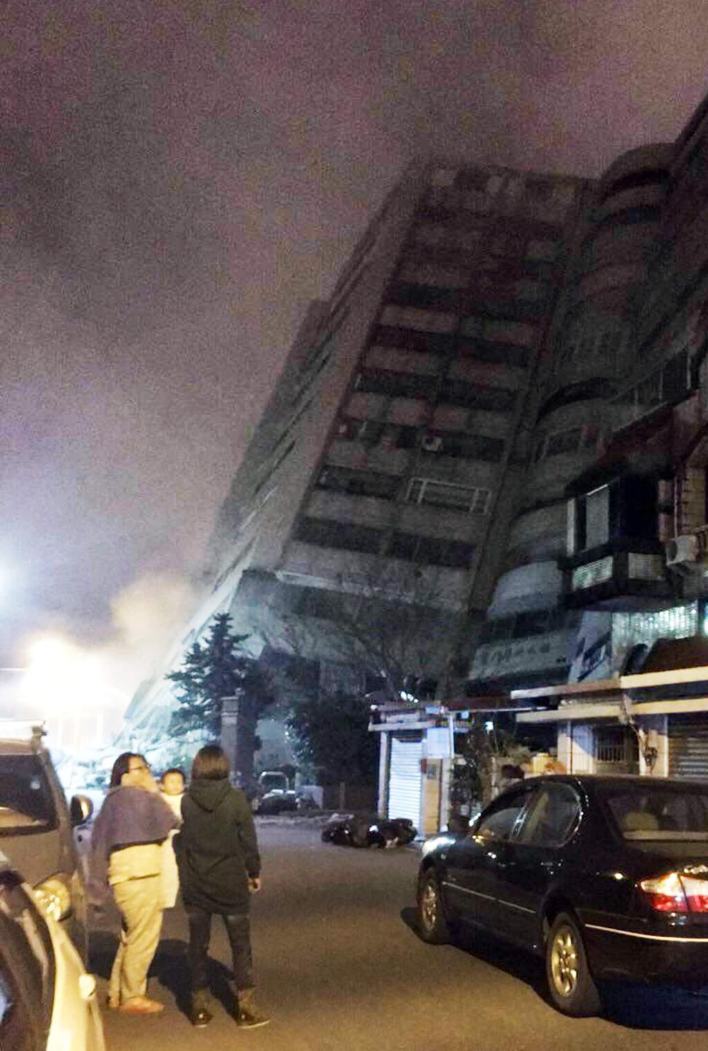 In this photo released by Hualien County Fire Bureau, Taiwanese people watching a building that collapsed on its side from an early morning earthquake in Hualien County, eastern Taiwan, early Wednesday, Feb. 7 2018. A 6.4-magnitude earthquake has struck eastern Taiwan, according to the U.S. Geological Survey. (Hualien County Fire Bureau via AP)