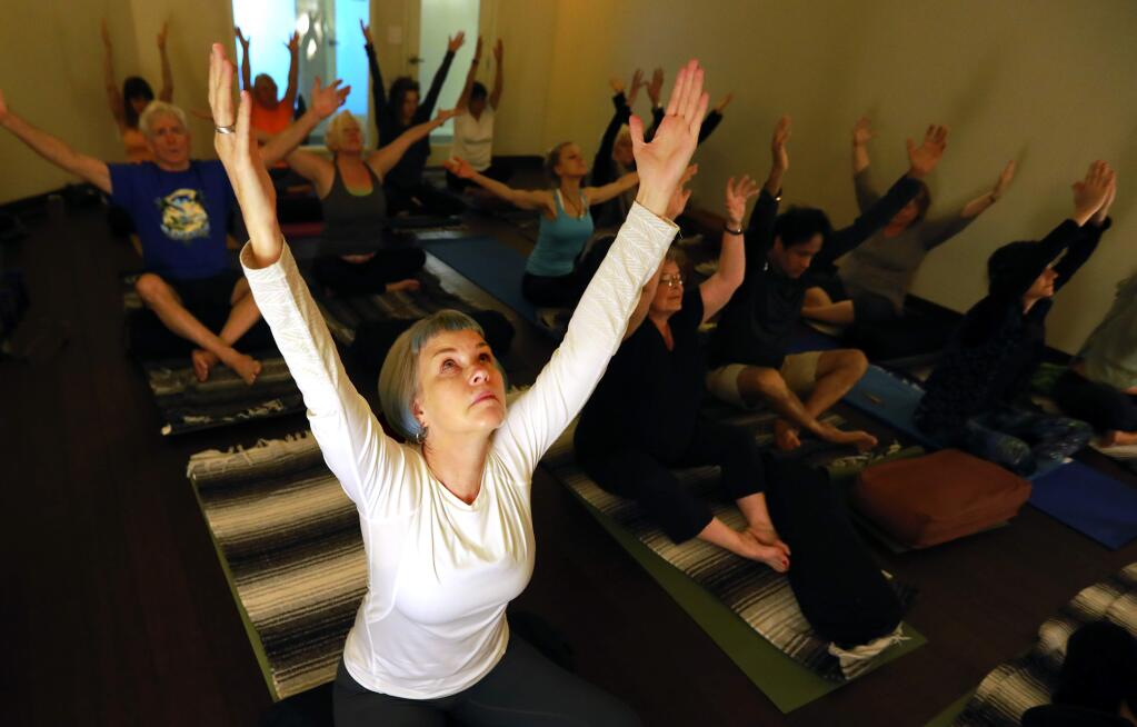 Michelle Morey, front, participates in a Trauma-Informed Yoga and iRest Meditation class at YogaOne in Santa Rosa on Saturday. The classes are offered to help fire survivors recover, both physically and emotionally, from the recent wildfires. Morey lost her home in Coffey Park last October. (photo by John Burgess/The Press Democrat)