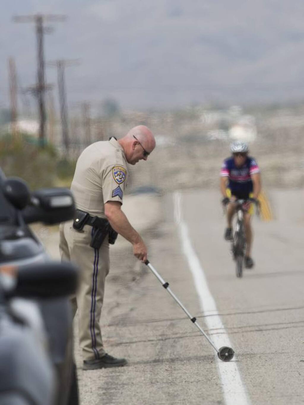 California Highway Patrol investigator takes measurements at the scene where a vehicle struck two cyclists participating in the 2018 Tour de Palm Springs near Indio Hills, Calif., Saturday, Feb. 10, 2018. Police say the car seen was driving down a road at twice the speed limit colliding into cyclists participating in the 100-mile charity bike ride. (Omar Ornelas/The Desert Sun via AP )