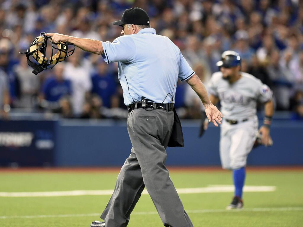 Home plate umpire Dale Scott, left, signals for Texas Rangers' Rougned Odor to score after conferring with the base umpires to confirm an error by Toronto Blue Jays catcher Russell Martin (not shown) on the play during the seventh inning in Game 5 of baseball's American League Division Series, Wednesday, Oct. 14, 2015 in Toronto. (Frank Gunn/The Canadian Press via AP) MANDATORY CREDIT