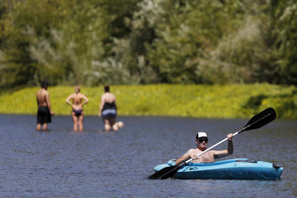 Greg Hill kayaks past swimmers wading in the Russian River at Del Rio Woods Beach on Sunday, July 28, 2013 in Healdsburg, California. (BETH SCHLANKER/ The Press Democrat)