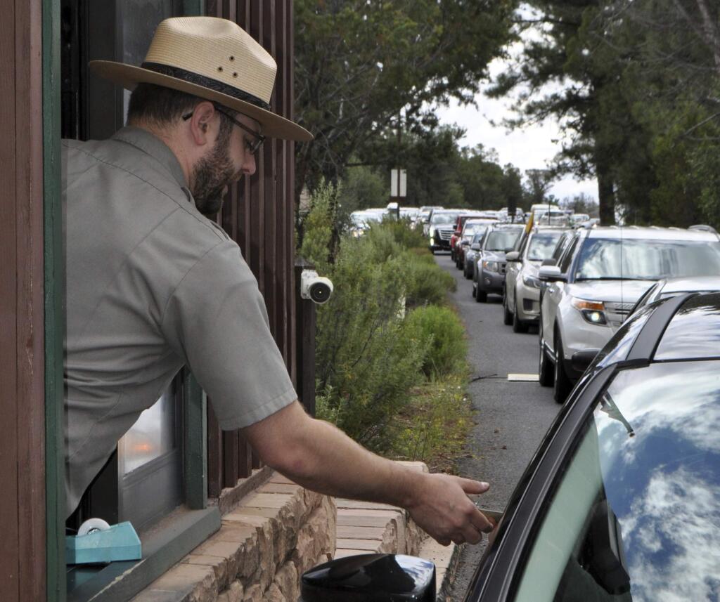 FILE--In this file photo taken Aug. 2, 2015, Nate Powell, an employee with Grand Canyon National Park, collects an entrance fee as traffic is backed up as vehicles arrive at an entrance gate at Grand Canyon National Park, Ariz. A new study concludes visitors may be steering clear of some U.S. national parks or cutting their visits short because of pollution.(Emery Cowan/Arizona Daily Sun via AP, file)