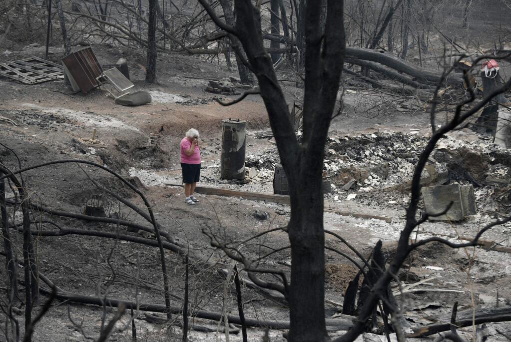 FILE- In this Aug. 9, 2018, file photo Loretta Root wipes her eyes while visiting the remains of her home in the Keswick area burned in a wildfire in Redding, Calif. More than 80 families who lost their homes in California's deadly Carr Fire in July have learned weeks or months later that their dogs and cats had survived the deadly disaster. A network of about 35 volunteers, called Carr Fire Pet Rescue and Reunification, is responsible for many of the happy endings and continues to track and catch missing pets nearly two months after the fire was extinguished. (AP Photo/John Locher, File)
