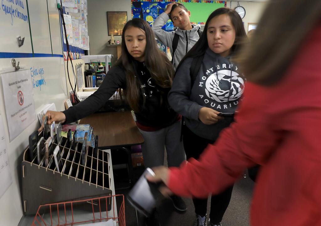 From left, Ashley Flores Rodriguez, Omar Espinoza Hernandez and Kristie Castillo, take their phones from a phone rack, Tuesday, Oct. 2, 2018, at Roseland Accelerated Middle School in Santa Rosa. Teacher Michael Healy came up with the idea so students wouldn't be tempted to use their devices during class. (Kent Porter / The Press Democrat) 2018