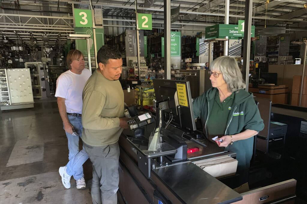 Cashier Lorna Pine, right, checks out customers at Sonoma's Friedman's Home Improvement, which remained open with limited electricity from a backup generator in Sonoma, Calif., Wednesday, Oct. 9, 2019. Employees escorted customers through the darkened store with flashlights and headlamps. Pacific Gas & Electric has cut power to more than half a million customers in Northern California hoping to prevent wildfires during dry, windy weather throughout the region. (AP Photo/Terry Chea)