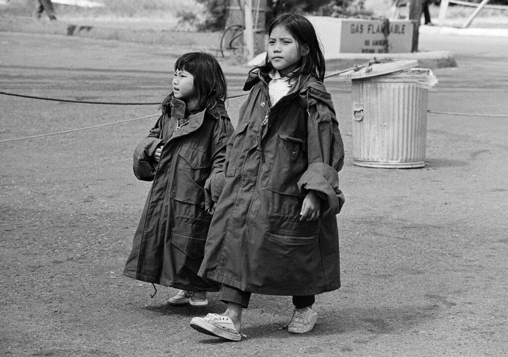Two young Vietnamese refugees wear oversized GI issue coats as they stroll the streets of their tent-city at the Camp Pendleton Marine Corps base in Southern California on May 7, 1975. Most refugees complain of the cold, but temperatures have been in the 60's and low 50's, much cooler then the warm days and nights in Vietnam. (AP Photo/Nick Ut)