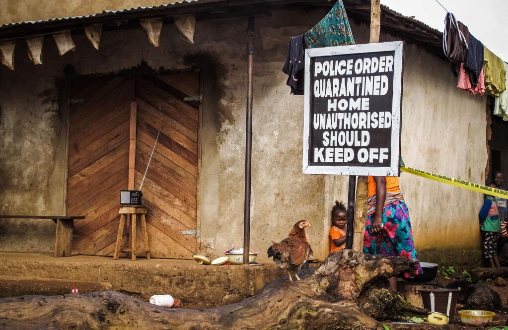 In this Wednesday, Oct. 22, 2014 file photo, a child stands near a sign advising of a quarantined home in an effort to combat the spread of the Ebola virus in Port Loko, Sierra Leone. More than 10,000 people have been infected with Ebola, according to figures released Saturday, Oct. 25, 2014 by the World Health Organization, as the outbreak continues to spread. Of those cases, 4,922 people have died. (AP Photo/ Michael Duff, File)