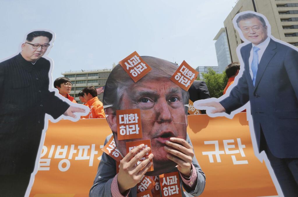 A protester wearing a mask of U.S. President Donald Trump, center, performs with cut-out photos of North Korean leader Kim Jong Un and South Korean President Moon Jae-in, right, during a rally against the United States' policies against North Korea near the U.S. embassy in Seoul, South Korea, Friday, May 25, 2018. (AP Photo/Ahn Young-joon)