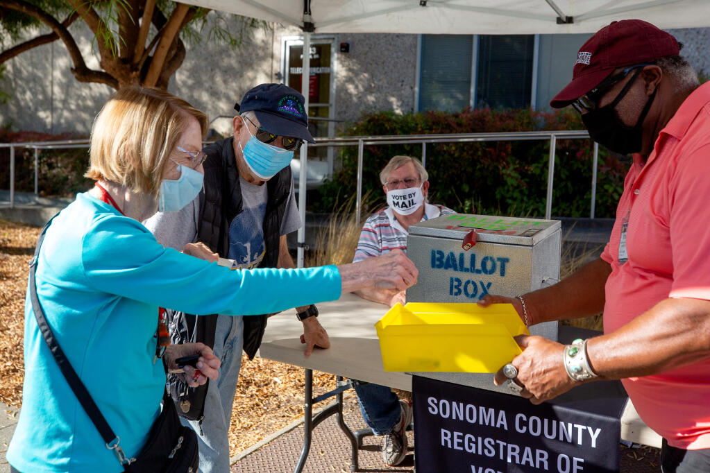 Carol and Doug Lightfoot, left, of Rincon Valley, take their "I Voted" stickers from a bin held by election worker Andre Dews after placing their ballots inside the ballot box at the Sonoma County Registrar of Voters office in Santa Rosa on Tuesday, Oct. 13, 2020. (Alvin A.H. Jornada / The Press Democrat)