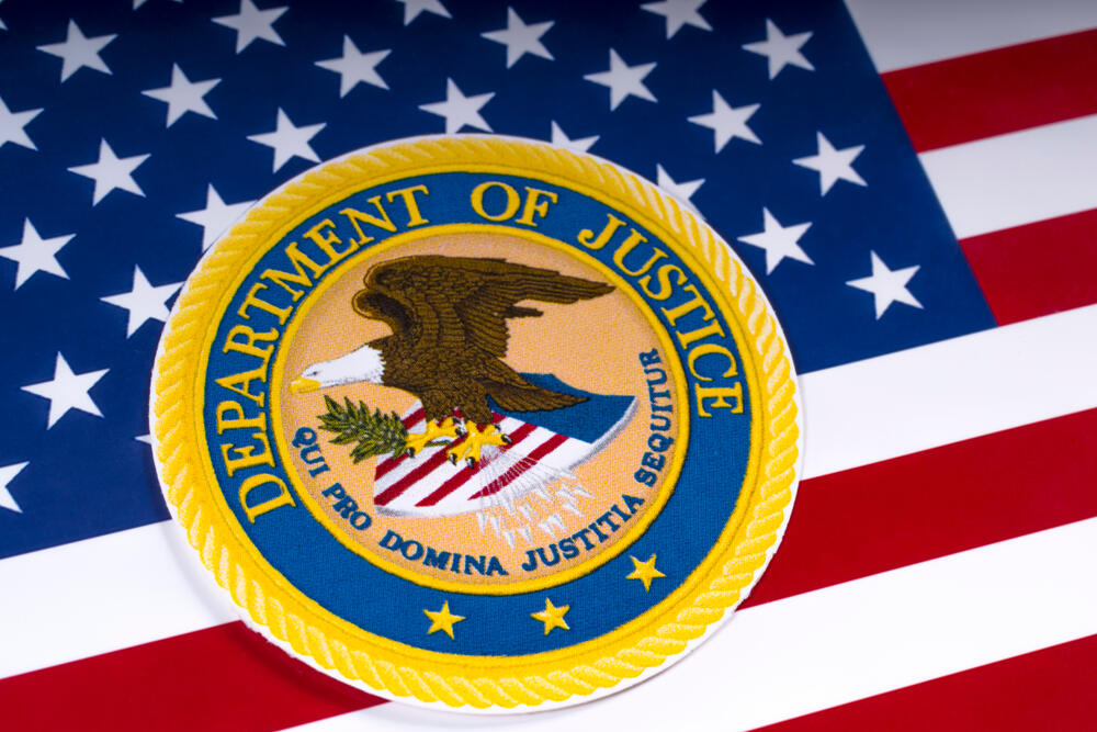 MARCH 26TH 2018: United States Department of Justice DOJ seal portrayed with the US flag (Chris Dorney / Shutterstock)