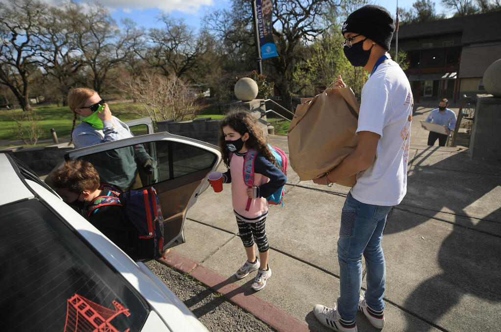 Boys and Girls Club staffer Pradbe Watthnnawes carries prepared food to Katie Estupian and her children, Enzo, 8, left, and Fiona, 6, Friday, March 5, 2021, in Sonoma. The food was prepared by Elaine Bell Catering, after a wedding was canceled and the couple to be married donated $20,000 worth of food to go to various organizations that help people in need. (Kent Porter / The Press Democrat) 2021