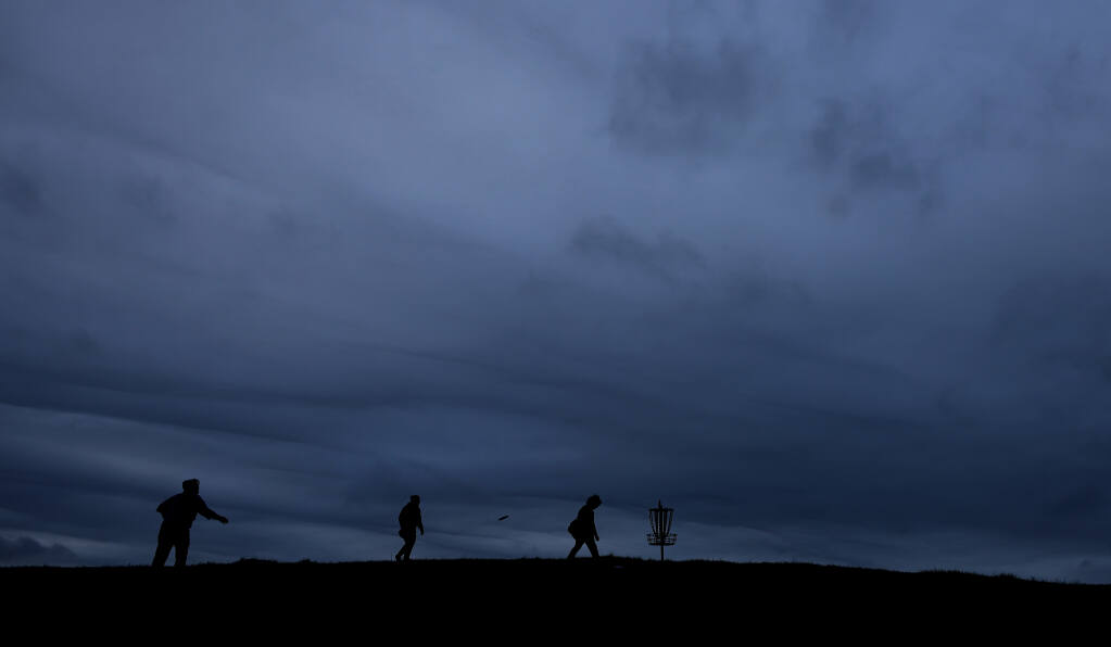 From left, brothers Kiernan and Gavin Edwards join Caleb Slight for a round of disc golf as storm clouds move in above Crane Creek Regional Park, Saturday, March 12, 2022 near Rohnert Park. (Kent Porter / The Press Democrat)