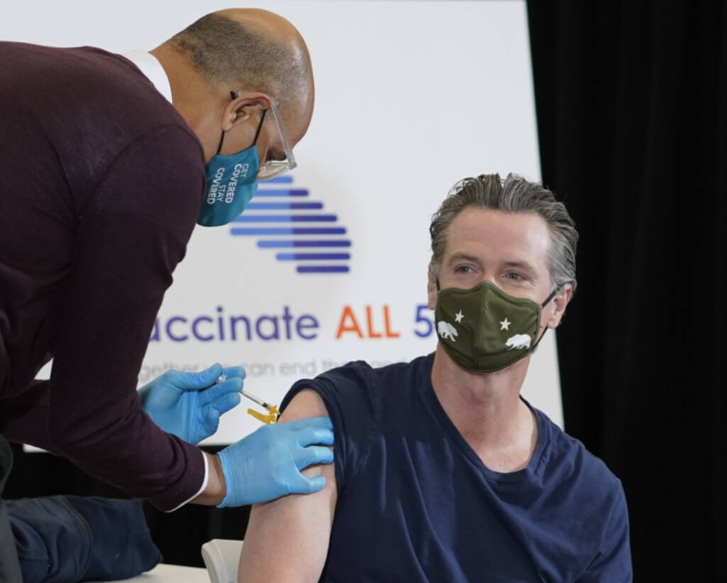 Dr. Mark Ghaly, Secretary, California Health and Human Services, left, inoculates California Gov. Gavin Newsom, right, at the Baldwin Hills Crenshaw Plaza in Los Angeles Thursday, April 1, 2021. Newsom was vaccinated with the new one-dose Janssen COVID-19 vaccine by Johnson & Johnson. (AP Photo/Damian Dovarganes)