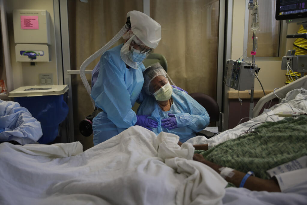 FILE - In this July 31, 2020, file photo, Romelia Navarro, right, is comforted by nurse Michele Younkin as she weeps while sitting at the bedside of her dying husband, Antonio, in St. Jude Medical Center's COVID-19 unit in Fullerton, Calif. (AP Photo/Jae C. Hong, File)