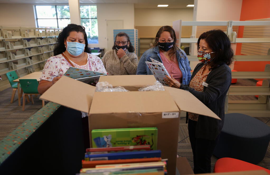 Senior library associate Marlene Vera, right, shows children's books to community members Marisol Angeles, Maria Saldivar, and Concepcion Dominquez at the new Roseland Regional Library in Santa Rosa on Friday, July 2, 2021.  (Christopher Chung/ The Press Democrat)