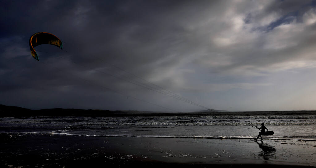 Sam Geller of Santa Rosa, 67, takes advantage of a break in storms - as a severe warned thunderstorm rumbles over Point Reyes in the background - to kite surf at Doran Regional Park in Bodega Bay, Tuesday, Jan. 10, 2023. (Kent Porter / The Press Democrat) 2023