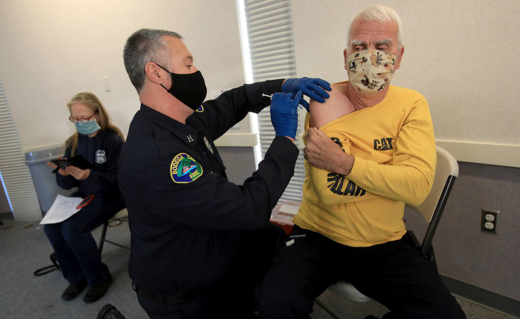 Monte Rio Fire Protection District chief Steve Baxman receives a COVID-19 vaccine from Bodega Bay Fire captain/EMT David Bynum, as firefighter/RN Gabriela Gibson, also with Monte Rio, waits for her inoculation, Wednesday, Dec. 23, 2020 in Santa Rosa. (Kent Porter / The Press Democrat)