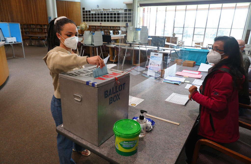 Anna Deurloo, left, drops off an absentee ballot for another voter before filling out her own ballot, as Carmen Marin watches, at the El Molino High School library polling location in Forestville on Tuesday, March 2, 2021. (Christopher Chung / The Press Democrat)