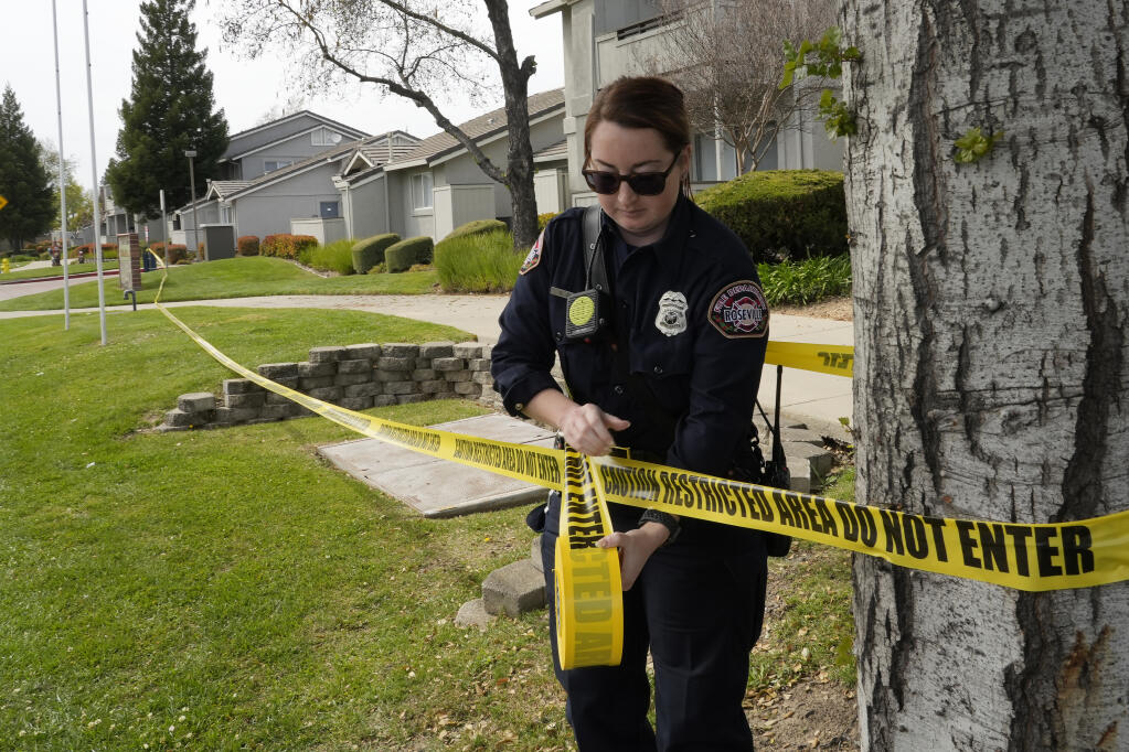 Roseville Fire Inspector Chelsea Zinc puts up barrier tape across the street from a local fitness center and library where a lockdown occurred in response to a possible shooting in Roseville, Calif., Thursday, April 6, 2023. At least three people were hospitalized and a suspect was taken into custody Thursday after a possible shooting in Northern California. (AP Photo/Rich Pedroncelli)