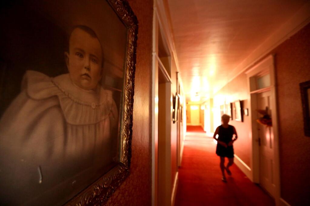ALTURAS, CA — MAY 17, 2023 — Terri LeDoux makes her way to her room past a series of framed vintage photos inside the historic Niles Hotel in Alturas, California, on May 17, 2023. The Niles Hotel in Alturas, California was constructed in 1908 as the Curtis Hotel. It was renamed the Niles Hotel in 1912, and in 1976 renovations began to restore the historic building to its former stature after decades of aging and neglect. The third floor of the hotel is believed to have a resident ghost, who is believed to be a former prostitute who was murdered in the hotel. It is alleged that she has been seen walking around the upper floors, and has even been known to hop into bed with male guests. (Genaro Molina / Los Angeles Times)