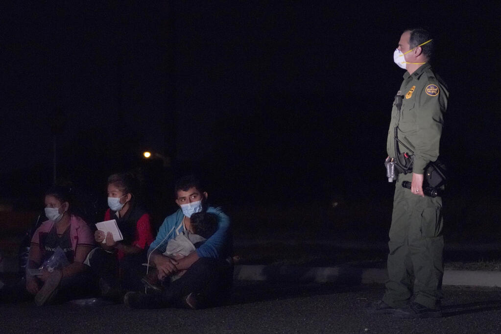 In this March 24, 2021 photo, a migrant man, center, holds a child as he looks at a U.S. Customs and Border Protection agent at an intake area after crossing the U.S.-Mexico border, early Wednesday, March 24, 2021, in Roma, Texas. The Biden administration said Monday that four families that were separated at the Mexico border during Donald Trump's presidency will be reunited in the United States this week in what Homeland Security Secretary Alejandro Mayorkas calls “just the beginning” of a broader effort. (AP Photo/Julio Cortez)