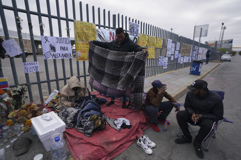 Protest signs cover the fence outside the Mexican immigration detention center that was the site of a deadly fire, as migrants wake up after spending the night on the sidewalk in Ciudad Juarez, Mexico, Thursday, March 30, 2023. (AP Photo/Fernando Llano)