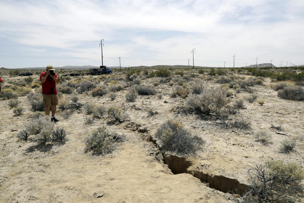 FILE - In this July 7, 2019 file photo, a visitor takes a photo of a crack in the ground following recent earthquakes in Ridgecrest, Calif., near the Naval Air Weapons Station China Lake military base. (AP Photo/Marcio Jose Sanchez, File)
